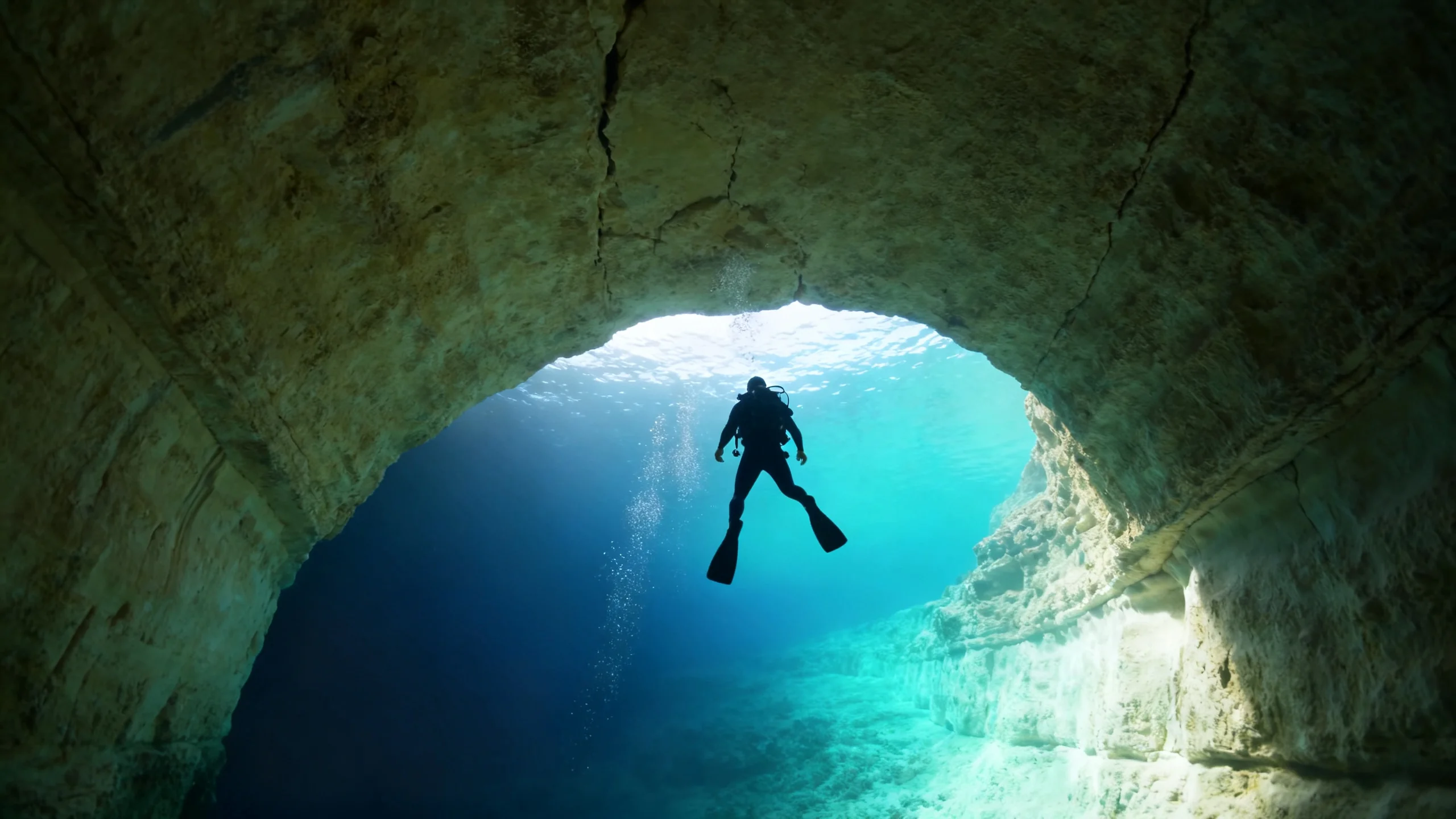 A diver descending into the Inland Sea tunnel at Dwejra, Gozo, with limestone walls and blue light