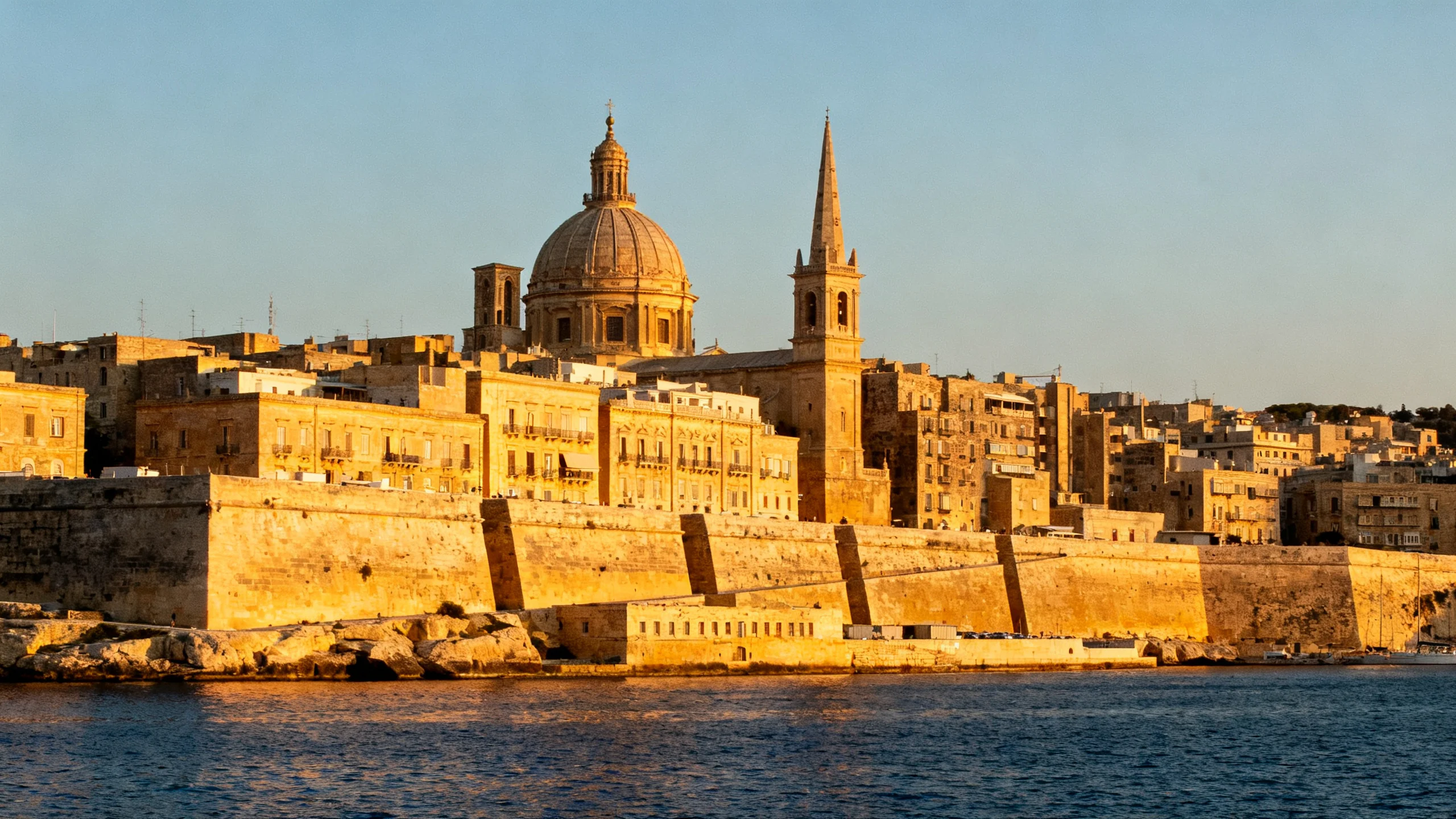 Valletta at golden hour viewed from across Grand Harbour, with the bastion walls dropping to the water