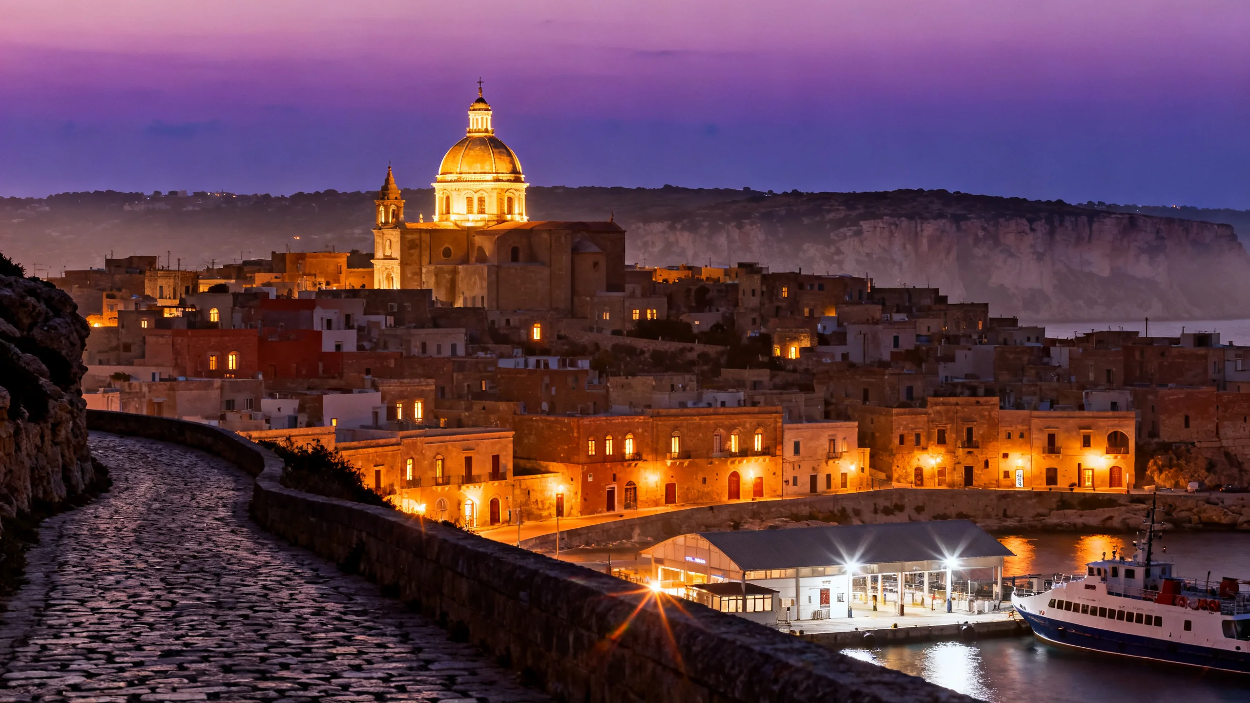 The Mellieha hilltop village at dusk, with the parish church dome and the path down toward the Cirkewwa-Comino ferry visible